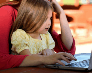 A young girl looking at a laptop screen with an adult