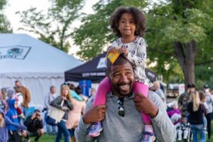 A Black dad smiling with his daughter on his shoulders