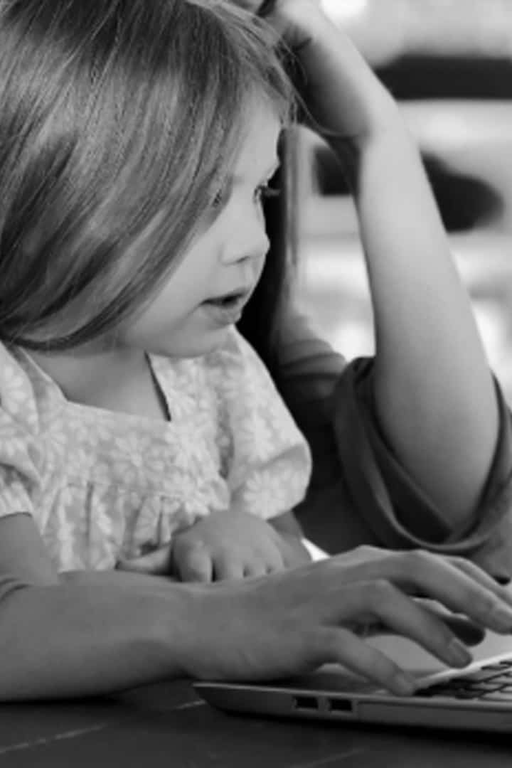A young girl looking at a laptop screen with an adult