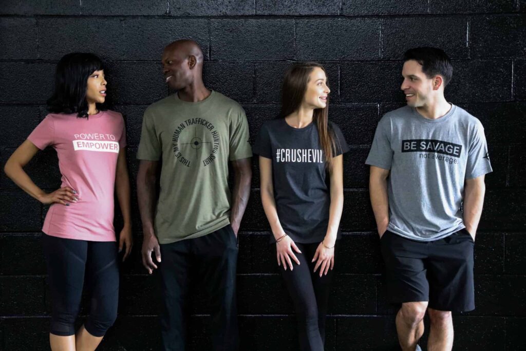 4 individuals wearing DeliverFund graphic tees leaning against a wall