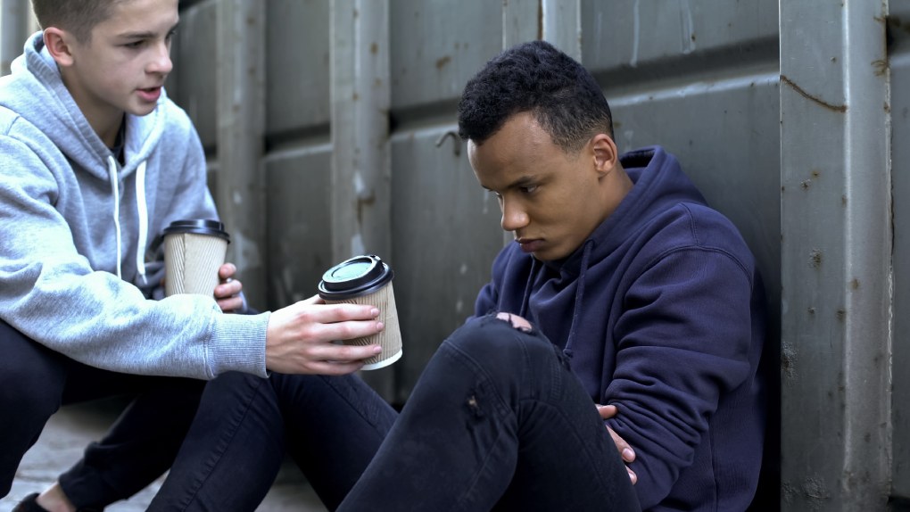 Boy sharing warm coffee with homeless man.