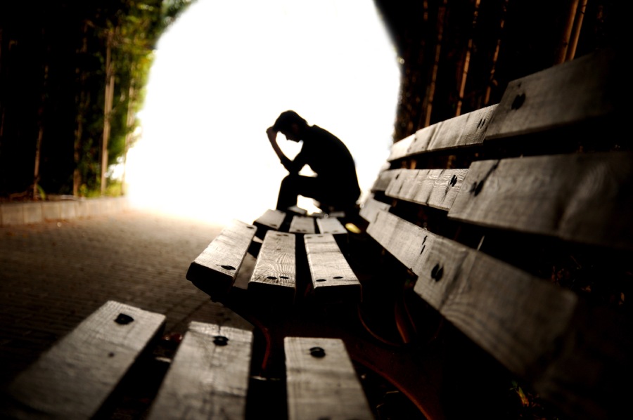 Depressed person sitting on roadside bench.