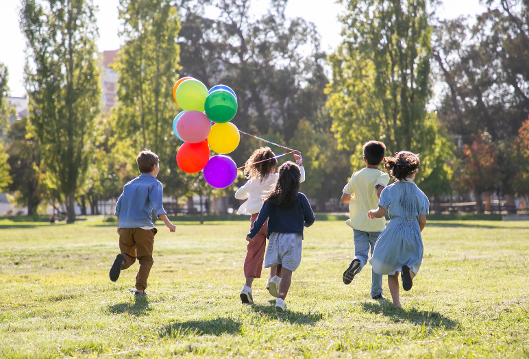 children running on field together, holding balloons